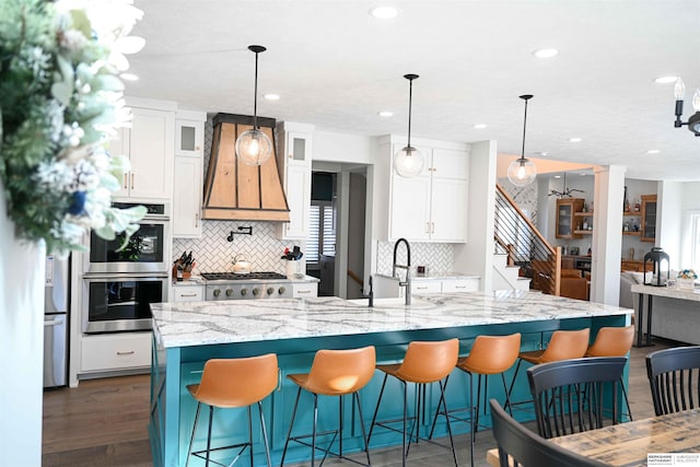 kitchen featuring stainless steel appliances, a sink, decorative backsplash, and premium range hood