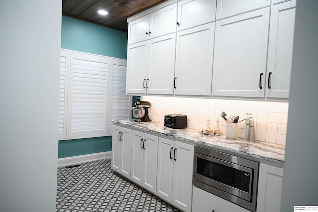 kitchen featuring light stone countertops, stainless steel microwave, decorative backsplash, and white cabinetry