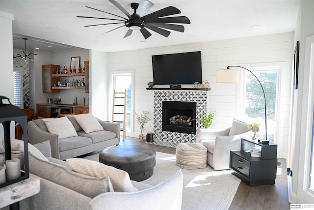 living room featuring a tile fireplace, wood finished floors, ceiling fan, and a bar