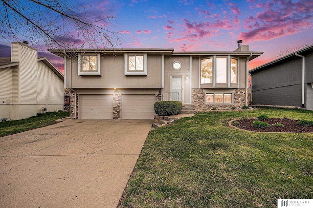 split foyer home featuring a front lawn, driveway, an attached garage, and stone siding