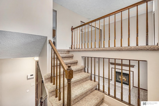 staircase with a tiled fireplace and a textured ceiling