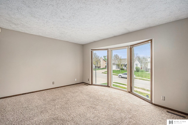carpeted empty room with a textured ceiling, visible vents, and baseboards