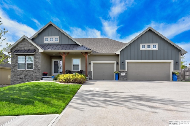 craftsman inspired home with board and batten siding, a standing seam roof, a front yard, a garage, and stone siding