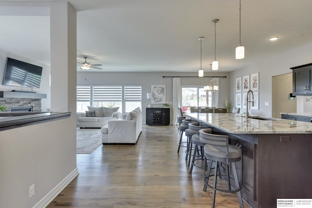 kitchen with wood finished floors, a fireplace, a kitchen bar, a sink, and ceiling fan with notable chandelier
