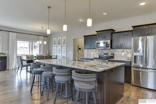 kitchen featuring decorative backsplash, a kitchen island with sink, a breakfast bar, light stone counters, and stainless steel appliances