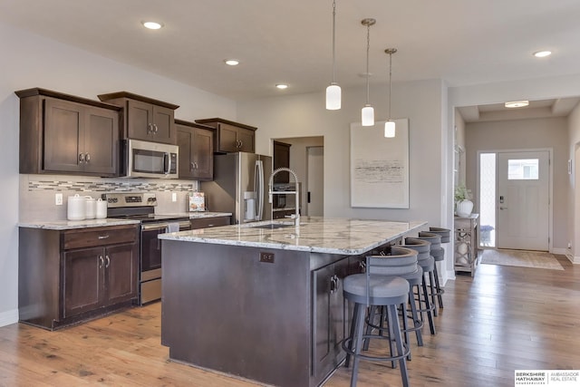 kitchen with light wood-type flooring, appliances with stainless steel finishes, dark brown cabinetry, and a center island with sink