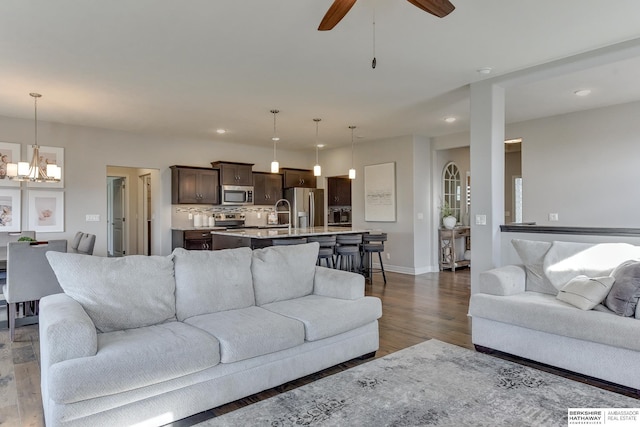 living room featuring recessed lighting, baseboards, wood finished floors, and ceiling fan with notable chandelier