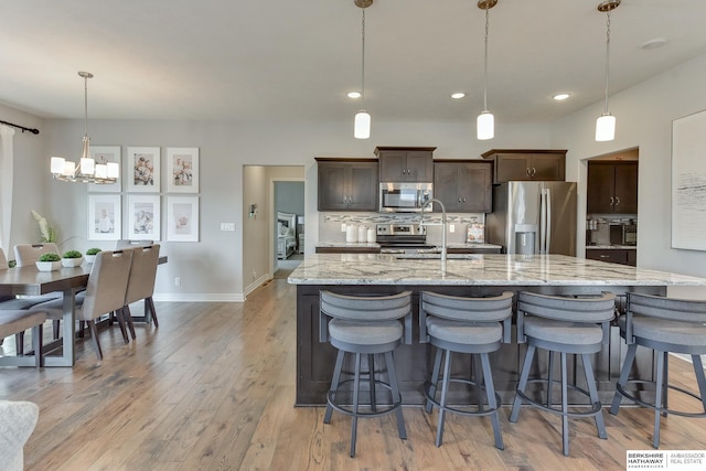 kitchen with dark brown cabinets, a center island with sink, a chandelier, a sink, and stainless steel appliances