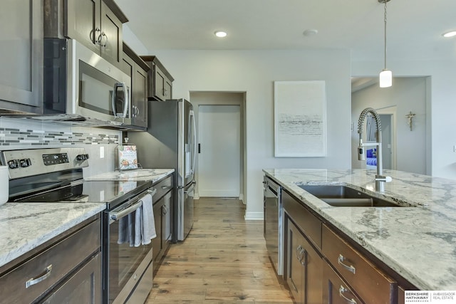 kitchen featuring stainless steel appliances, light stone counters, a sink, and light wood finished floors