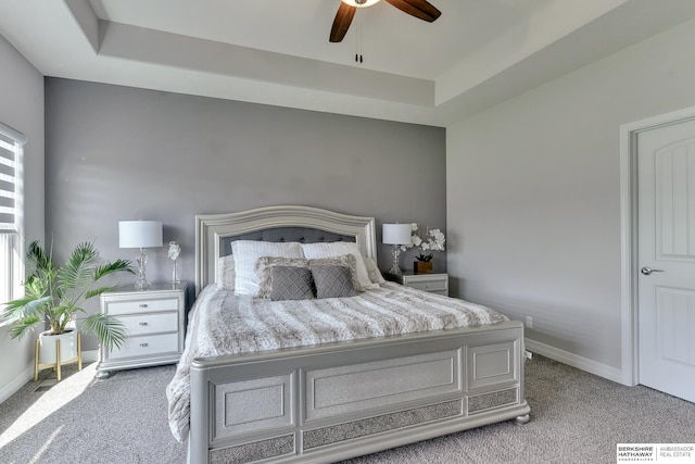 carpeted bedroom with a ceiling fan, baseboards, and a raised ceiling
