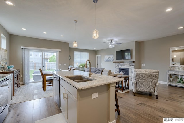 kitchen with a sink, a fireplace, a ceiling fan, hanging light fixtures, and wood finished floors