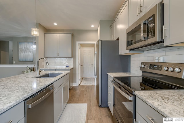 kitchen featuring hanging light fixtures, light wood-style flooring, decorative backsplash, appliances with stainless steel finishes, and a sink