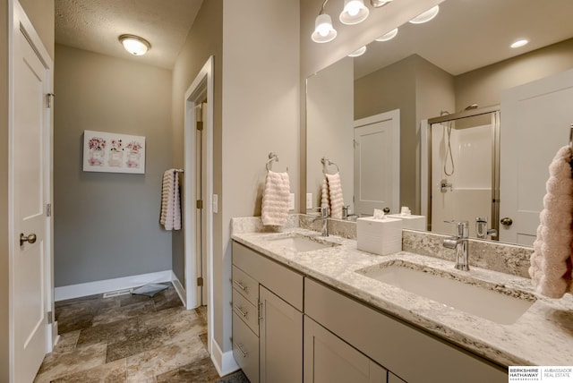 full bathroom featuring double vanity, baseboards, a stall shower, and a sink