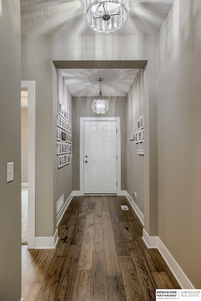 doorway to outside with visible vents, wood finished floors, a notable chandelier, and baseboards