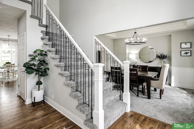 stairs with wood finished floors, a notable chandelier, and baseboards