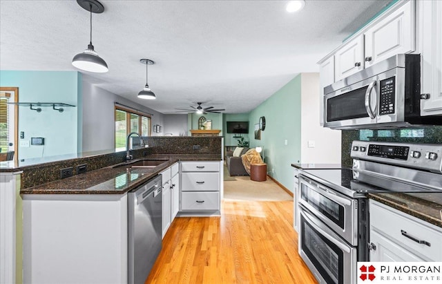 kitchen with a sink, stainless steel appliances, light wood-type flooring, pendant lighting, and white cabinets