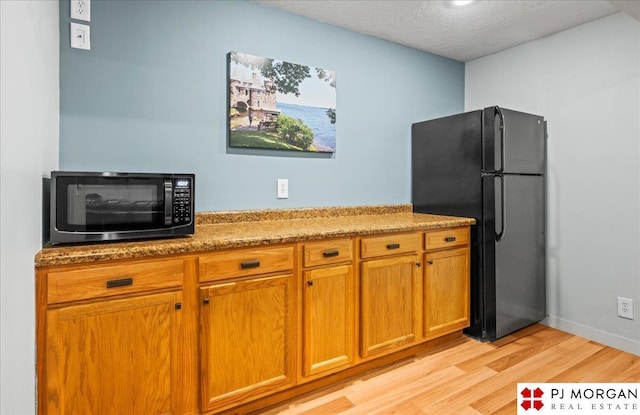 kitchen with brown cabinets, light wood-type flooring, black appliances, light stone counters, and a textured ceiling
