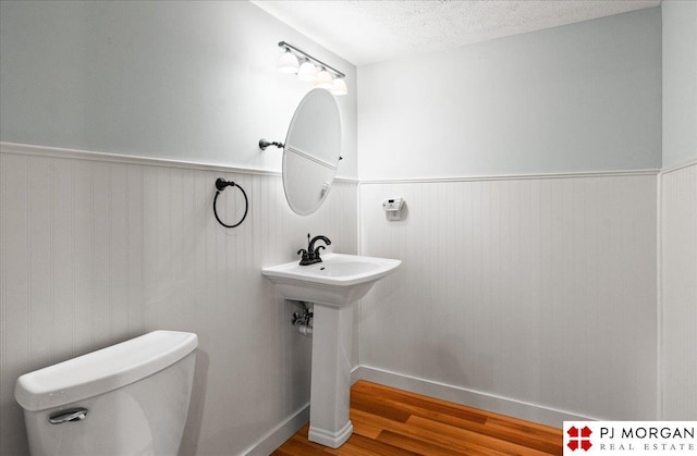 half bathroom featuring toilet, a textured ceiling, wainscoting, and wood finished floors