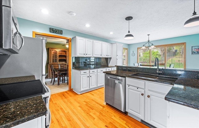 kitchen featuring decorative light fixtures, stainless steel appliances, white cabinets, and a sink