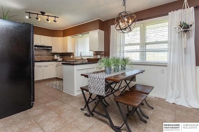 kitchen featuring black appliances, under cabinet range hood, dark countertops, a chandelier, and light tile patterned floors