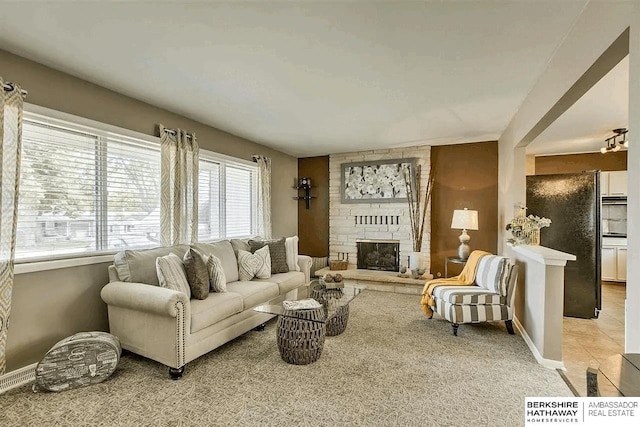living area featuring plenty of natural light, a stone fireplace, light carpet, and baseboards