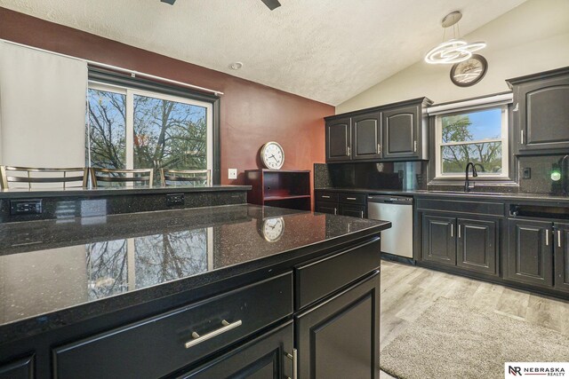 kitchen featuring a sink, light wood-type flooring, vaulted ceiling, stainless steel dishwasher, and a textured ceiling