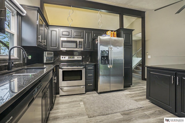kitchen featuring dark stone countertops, tasteful backsplash, light wood-style flooring, a sink, and appliances with stainless steel finishes