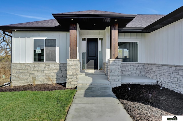 property entrance with board and batten siding, a shingled roof, and stone siding