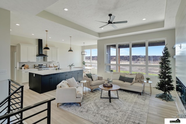 living area featuring ceiling fan, recessed lighting, a tray ceiling, and light wood-style floors