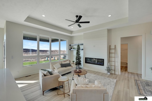 living area featuring light wood-type flooring, ceiling fan, a raised ceiling, and baseboards