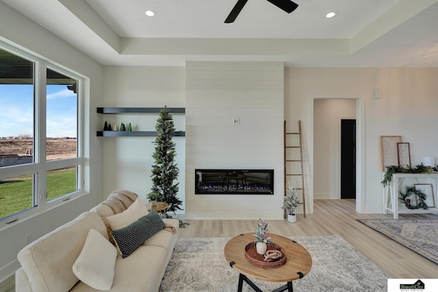 living room featuring recessed lighting, wood finished floors, ceiling fan, a fireplace, and a tray ceiling