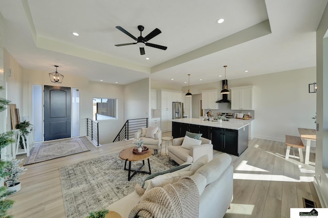 living room with a tray ceiling, light wood finished floors, a ceiling fan, and recessed lighting