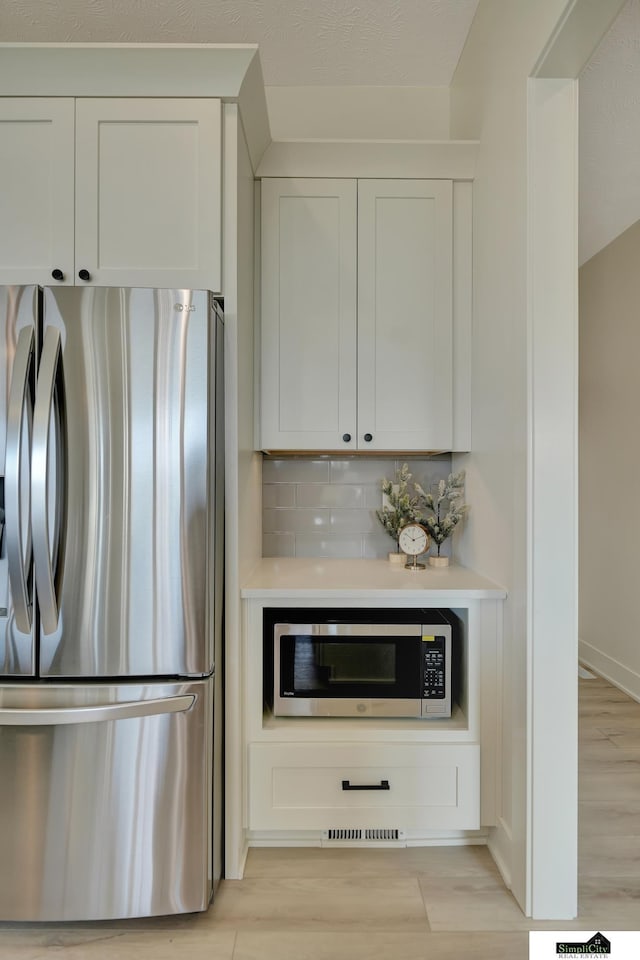 kitchen featuring light wood-type flooring, backsplash, light countertops, white cabinets, and appliances with stainless steel finishes