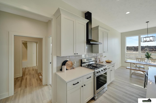 kitchen featuring tasteful backsplash, light countertops, gas stove, baseboards, and wall chimney exhaust hood