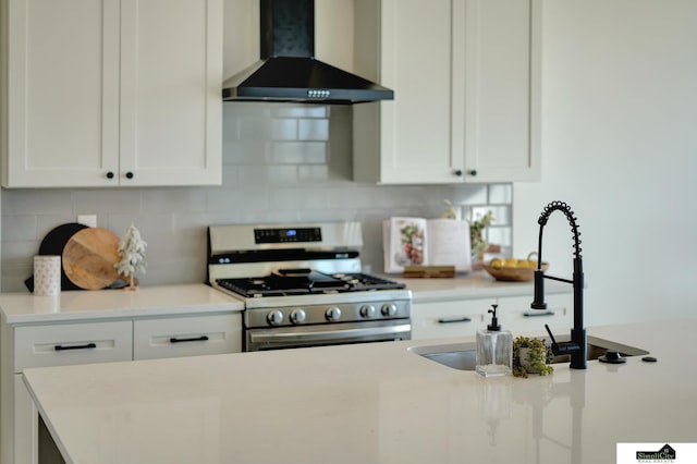 kitchen with wall chimney range hood, tasteful backsplash, white cabinets, a sink, and gas range