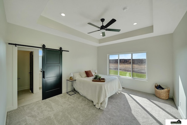 bedroom featuring a barn door, light carpet, baseboards, a raised ceiling, and a ceiling fan