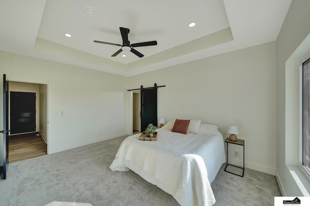 carpeted bedroom with recessed lighting, a barn door, ceiling fan, a raised ceiling, and baseboards
