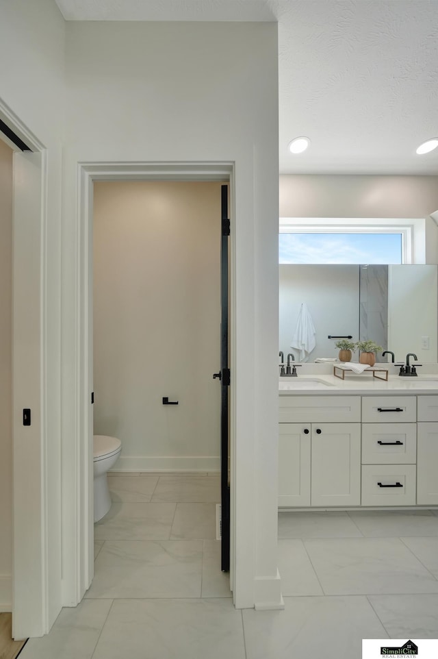 full bath with toilet, double vanity, and a sink