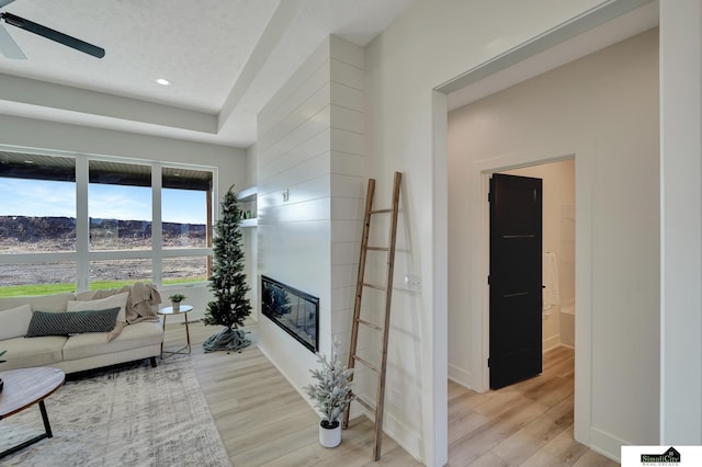 living room featuring recessed lighting, light wood-style floors, a glass covered fireplace, a ceiling fan, and baseboards