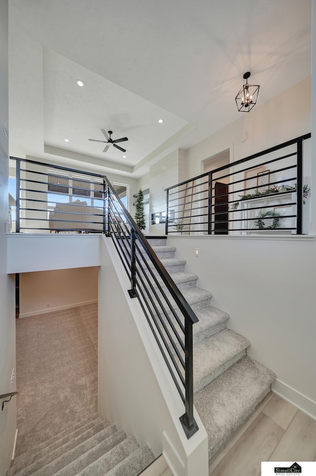 stairway featuring recessed lighting, baseboards, a raised ceiling, and a healthy amount of sunlight