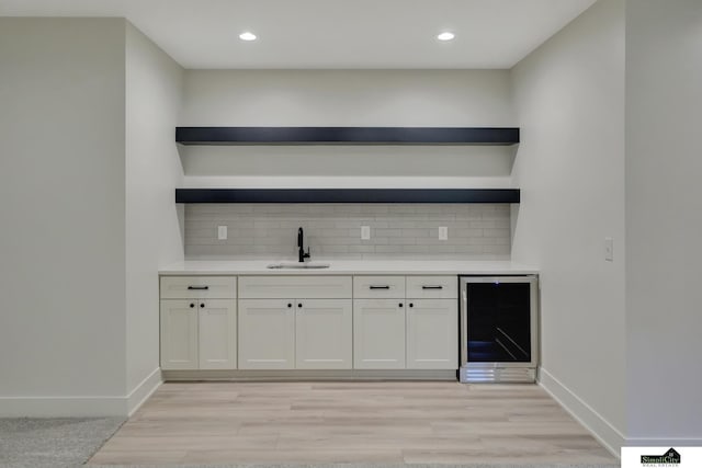 bar with beverage cooler, backsplash, light wood-style flooring, and a sink