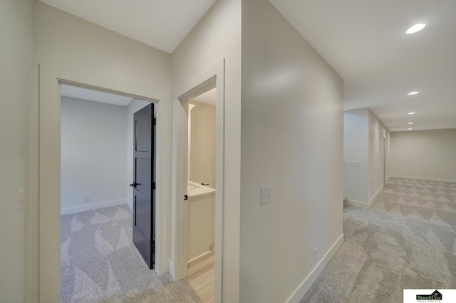 corridor with baseboards, recessed lighting, and light carpet