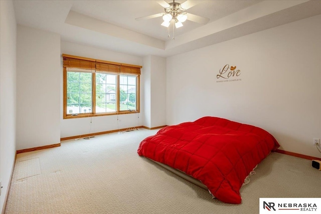 carpeted bedroom featuring baseboards, a raised ceiling, and ceiling fan
