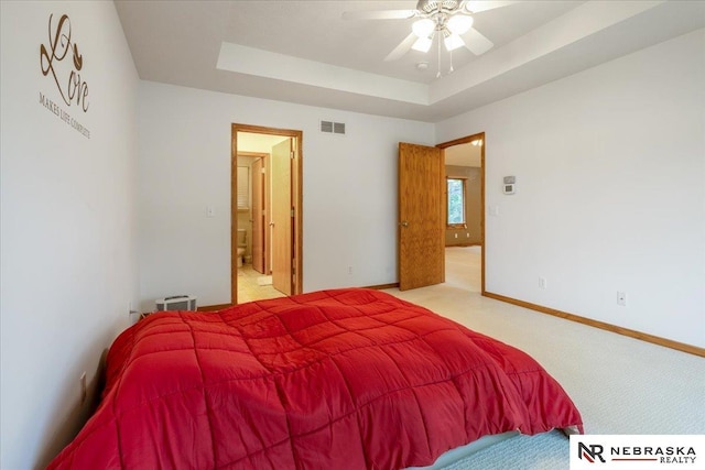 bedroom featuring light colored carpet, a tray ceiling, baseboards, and connected bathroom