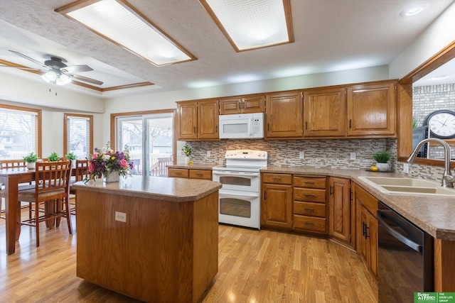 kitchen featuring a sink, brown cabinets, light wood-style floors, a center island, and white appliances