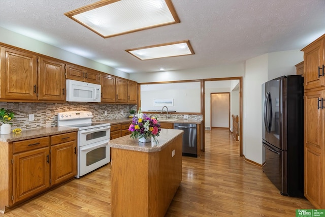 kitchen with light wood-style flooring, a sink, a center island, white appliances, and a peninsula