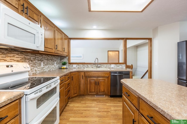 kitchen with light wood finished floors, a sink, brown cabinetry, backsplash, and white appliances