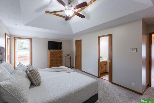 bedroom with connected bathroom, a tray ceiling, baseboards, light carpet, and a ceiling fan