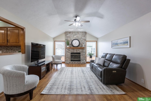 living room featuring a ceiling fan, light wood finished floors, lofted ceiling, and a brick fireplace