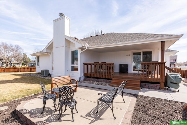 back of property with a wooden deck, a chimney, a patio area, central air condition unit, and fence